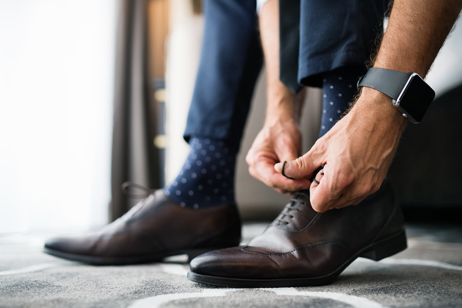 A man is putting on his formal shoes, tying the laces tightly.
